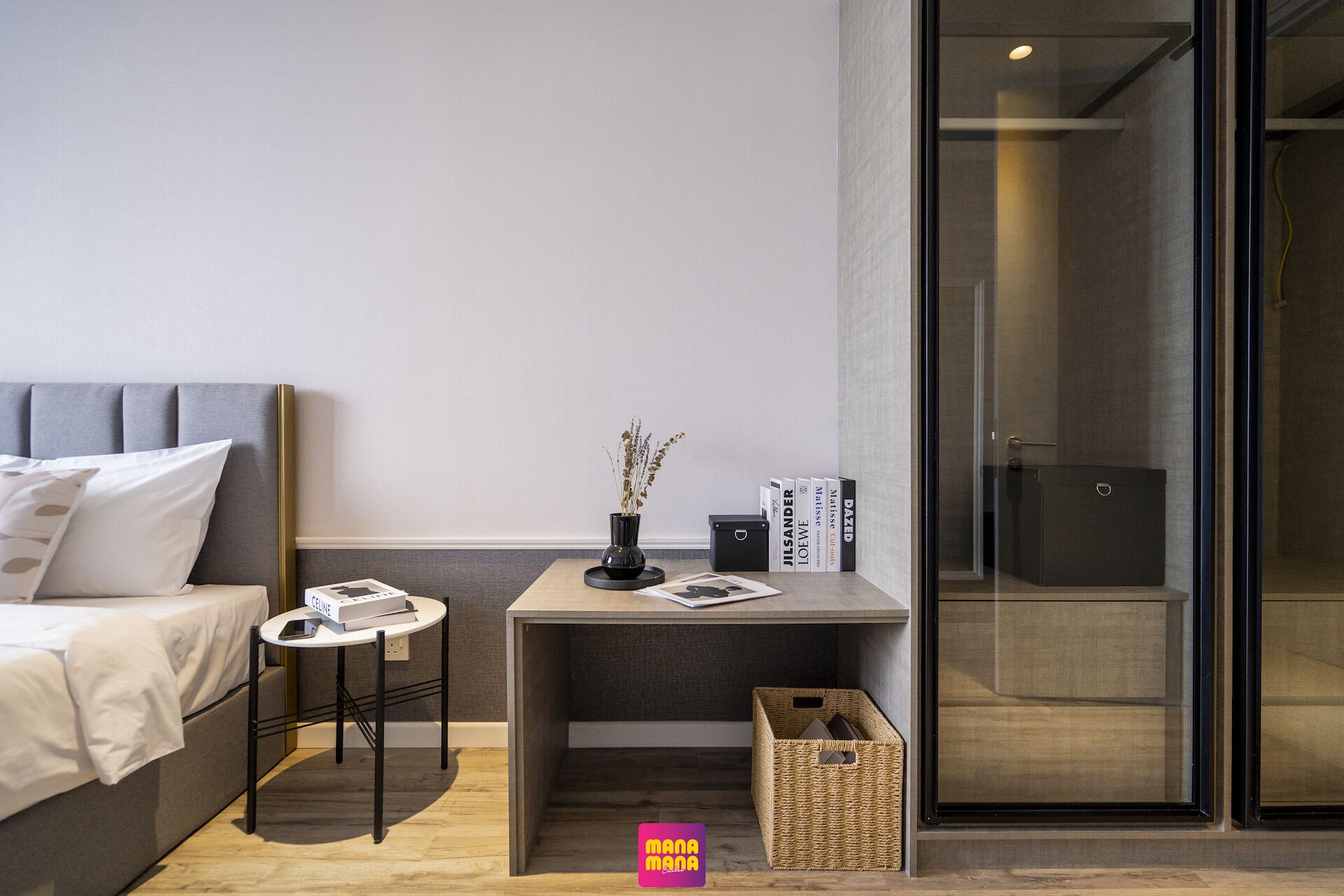 A modern bedroom with a bed, a small table with a vase, books, and a basket.