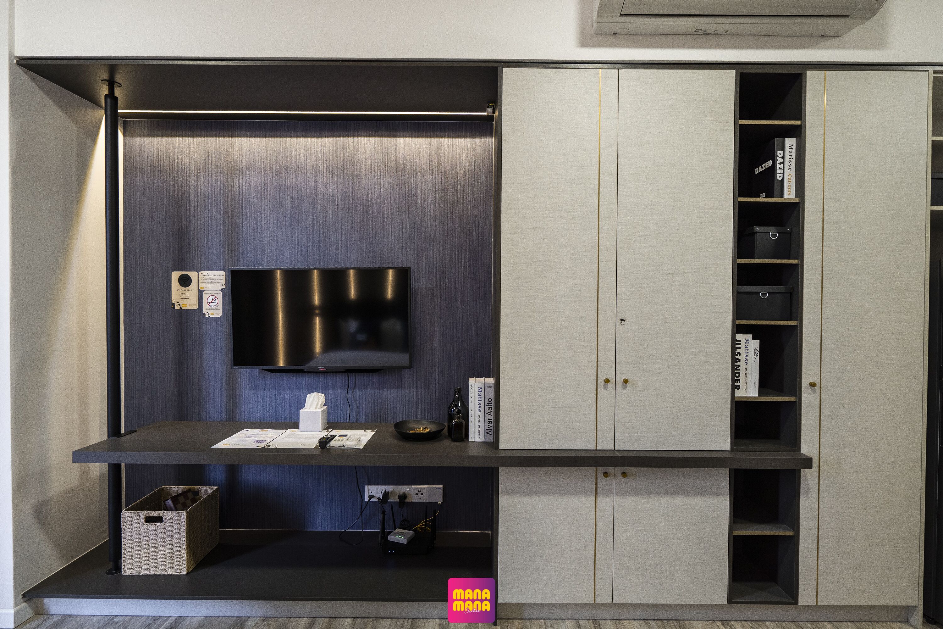 A modern, compact room with a built-in TV, a small table with a remote, and a storage cabinet with shelves.