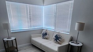 A modern living room with a white sofa, two side tables, and a large window with blinds.