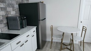 A modern kitchen with white cabinets, a black refrigerator, a built-in oven, and a round dining table with two chairs.