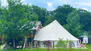 Een tent met een puntig dak en een kleinere aanleunconstructie, omgeven door weelderige begroeiing.