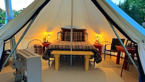 Een gezellige tent met een bed, een tafel en twee stoelen. Op de tafel staan een verwarming en een lamp.