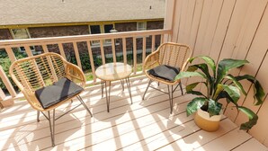 Une terrasse en bois avec des chaises et une table en osier, un pot de fleurs et, en arrière-plan, une vue sur un bâtiment en briques.