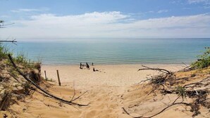 A beach with clear water, sandy dunes, and a few people in the distance.
