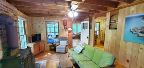 L’intérieur d’un chalet en bois, avec un canapé vert, un téléviseur, une cheminée et un ventilateur de plafond.