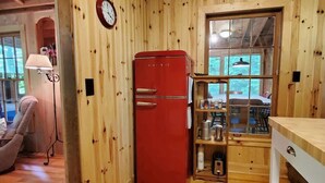 Un intérieur en bois avec un réfrigérateur rouge, une horloge et une fenêtre donnant sur une terrasse.