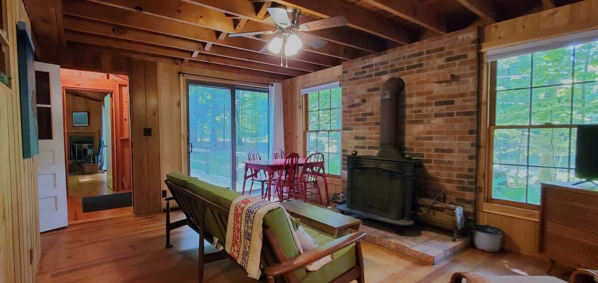 A cozy cabin interior with a fireplace, wooden floors, and large windows.