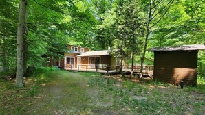 A cabin with a porch and a small shed in a wooded area.