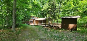 Une cabane avec une véranda et un petit abri de jardin, située dans une zone boisée.