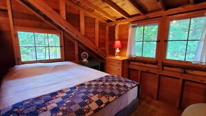 Une chambre confortable dans un chalet en bois, avec un lit, une table de chevet, une lampe et deux fenêtres avec des rideaux.