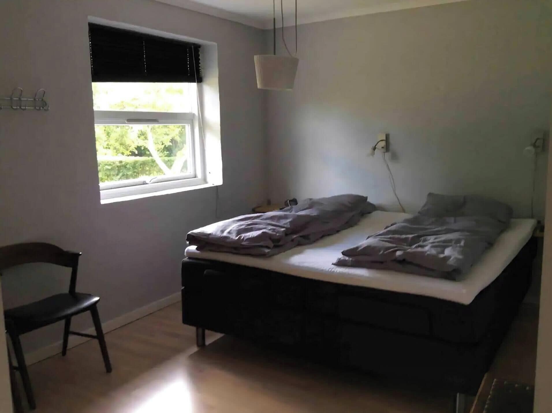 Une chambre avec un lit simple, une chaise, une fenêtre avec des stores et un luminaire suspendu.
