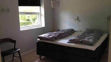Une chambre avec un lit simple, une chaise, une fenêtre avec des stores et un luminaire suspendu.