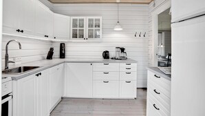 Una cocina moderna con armarios blancos, horno empotrado, cafetera y una lámpara colgante.