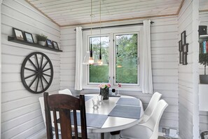 A dining area with a round table, chairs, a wooden chair, a wall-mounted wagon wheel, and a window with curtains.