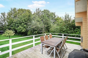A wooden deck with a table and chairs, surrounded by a white fence, overlooking a grassy area with trees. - 3 bedroom accommodation in Hundested (Hundested)