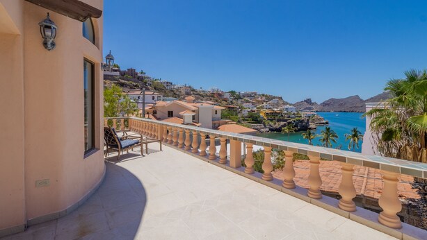A balcony with a view of the sea, a chair, and a railing.