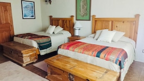 A room with two beds, a wooden chest, a nightstand with a lamp, and a framed picture on the wall.
