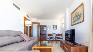 Una sala de estar moderna con un sofá gris, una mesa de centro, un televisor y un comedor con sillas azules y una mesa de madera.