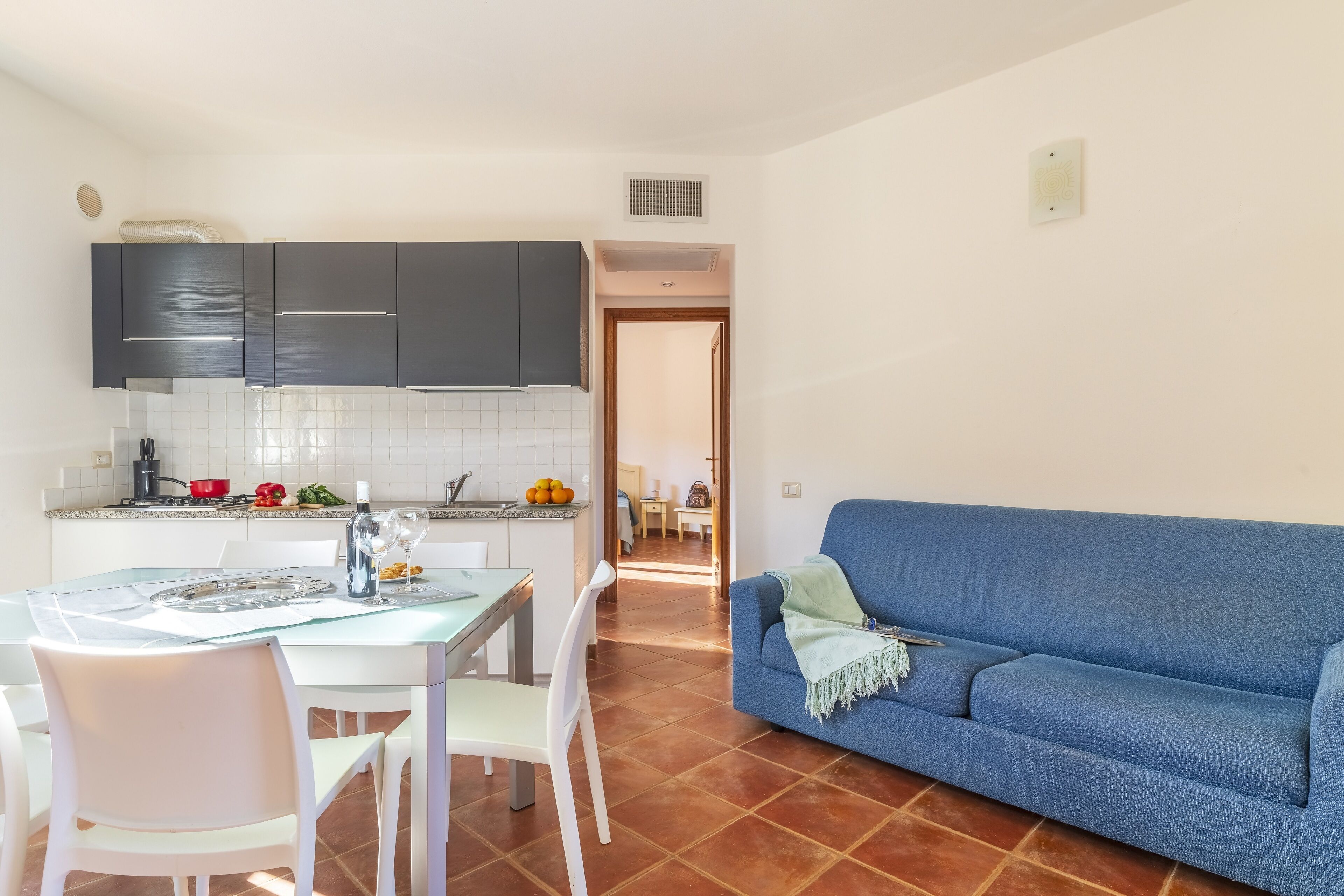 A modern kitchen with dark cabinets, a dining table with chairs, and a blue sofa in the living area.