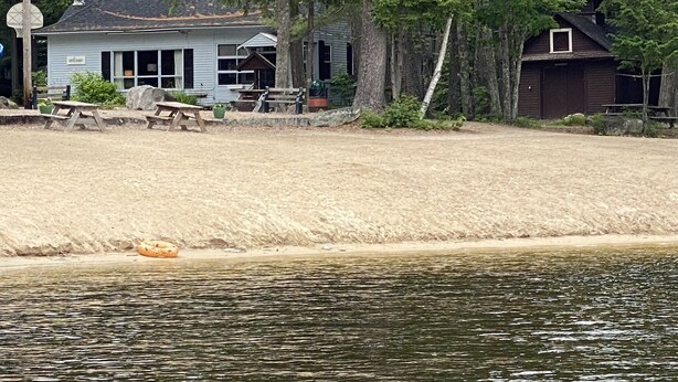 A lakeside property with a house, picnic tables, and a dock extending into the water.