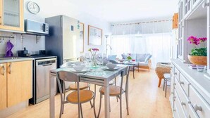 Une cuisine moderne dotée d’appareils électroménagers en acier inoxydable, un coin repas avec une table en verre et une vue sur le salon.