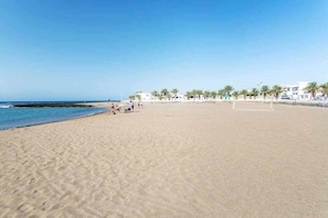 Een strand met heldere lucht, palmbomen en een gebouw op de achtergrond.