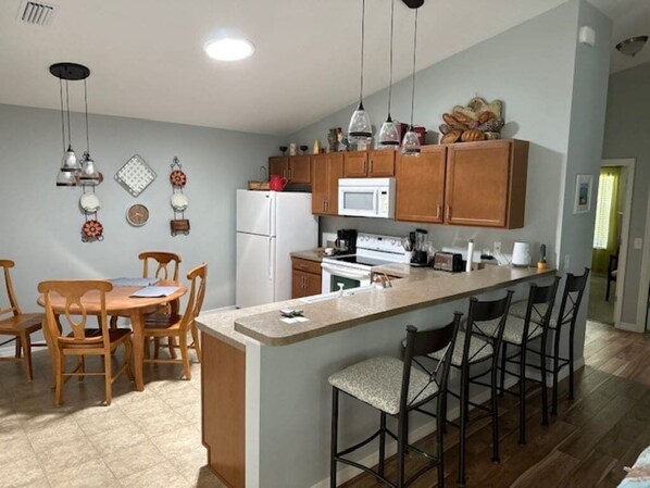 A kitchen with wooden cabinets, a white refrigerator, a microwave, and a bar area with stools. - 2 bedroom / 2 full bath with great location in The Villages! (The Villages)