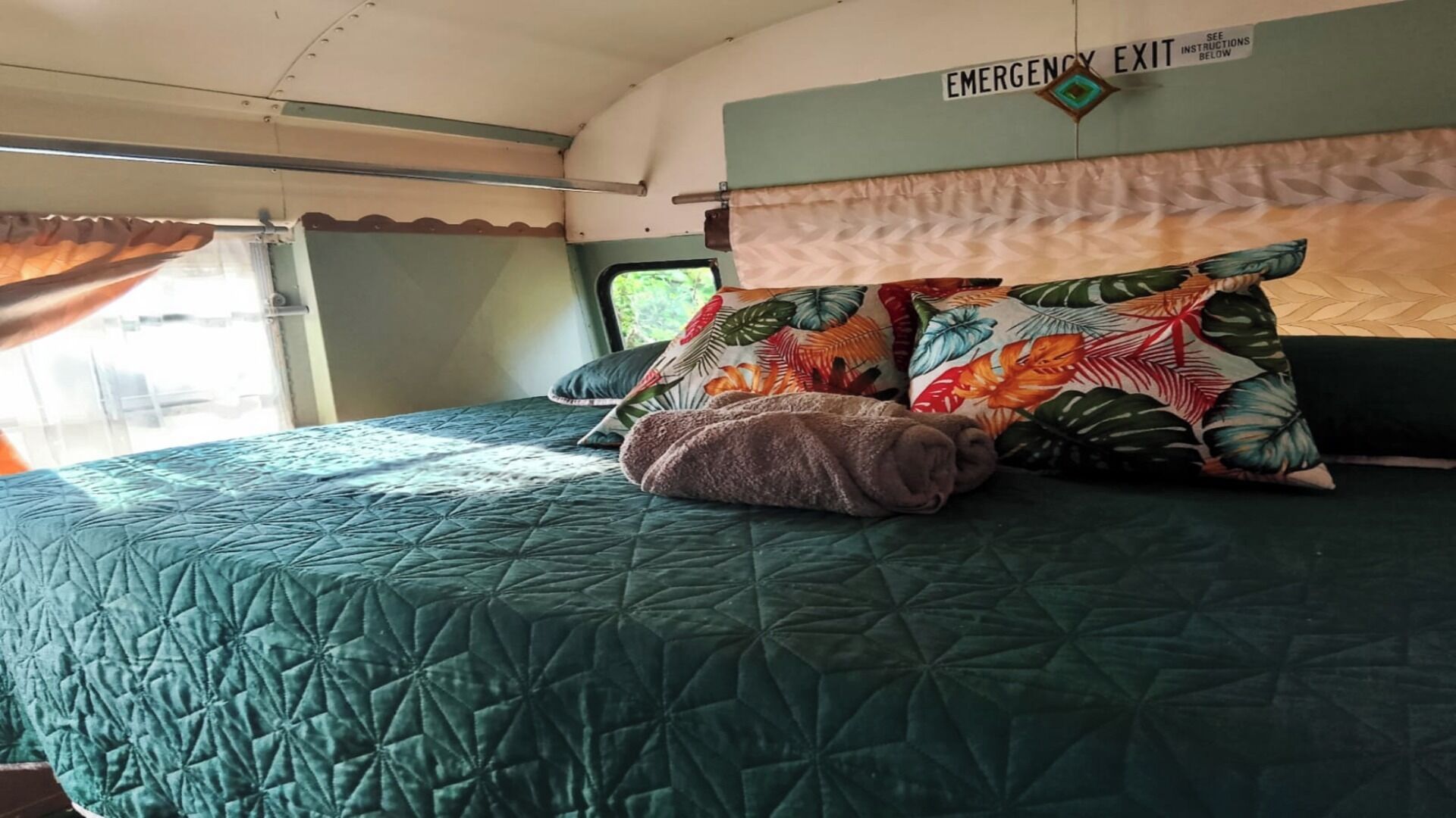 Un lit avec une couette verte, un coussin à motifs floraux et une couverture marron.