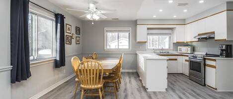 Une cuisine moderne avec un coin repas, des meubles blancs, un four encastré et un ventilateur de plafond.