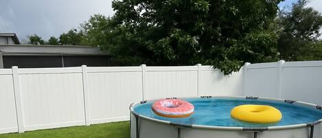 A backyard with a swimming pool, two inflatable rings, and a brick fire pit.