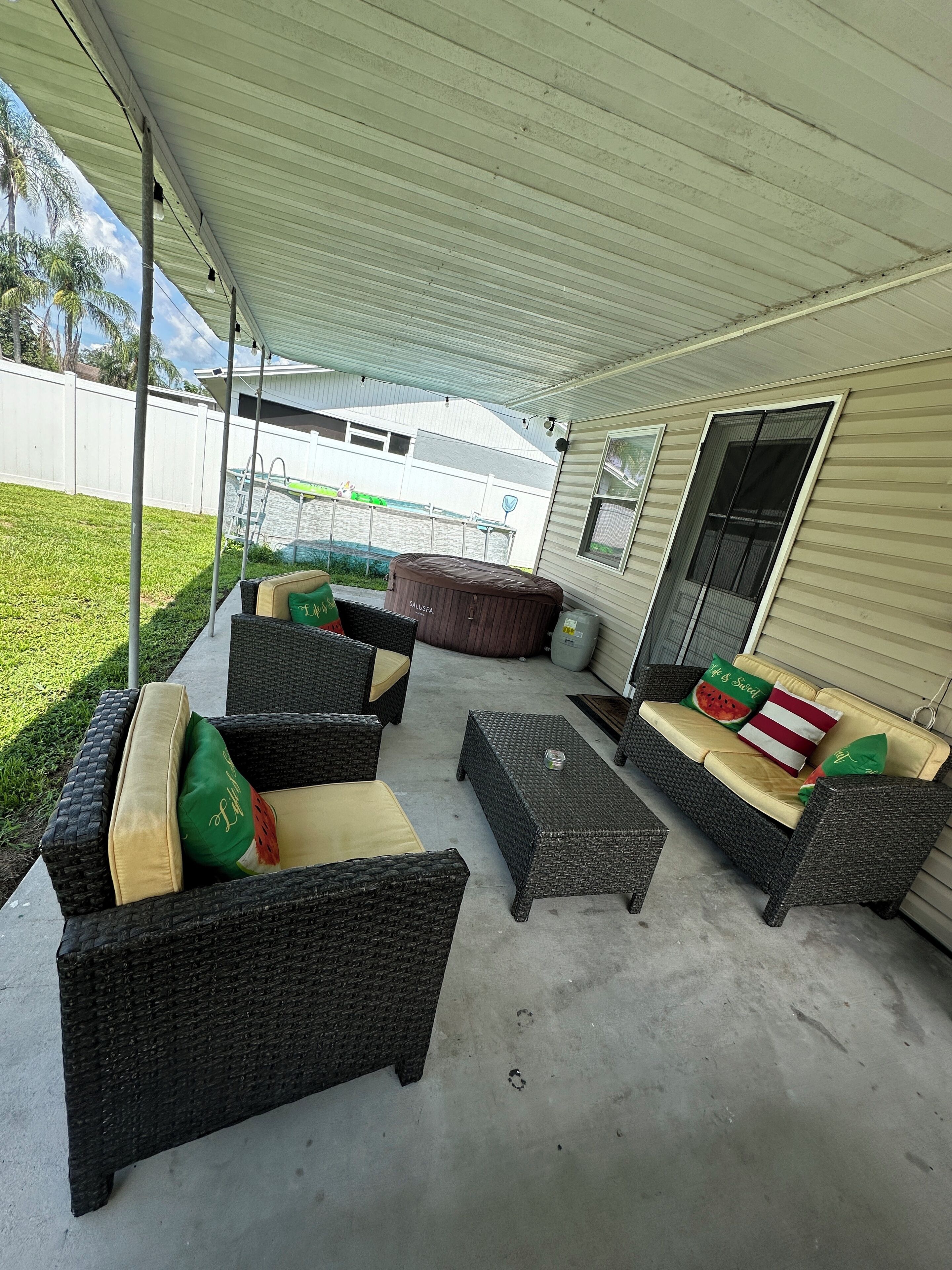 An outdoor patio area with wicker furniture, a hot tub, and a covered section.