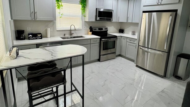 Una cocina moderna con armarios blancos, electrodomésticos de acero inoxidable y encimera de mármol.