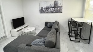 Una sala de estar moderna con un sofá modular, un televisor de pantalla plana, una mesita redonda y un taburete de bar.