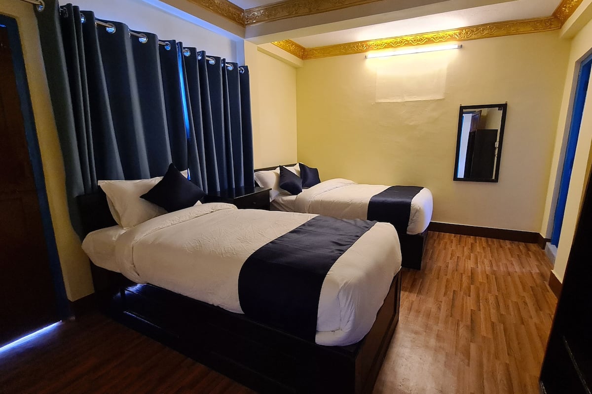 A hotel room with two beds, a wooden floor, a mirror, and a door.