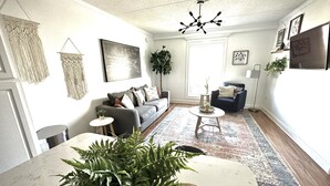 A living room with a grey sofa, a coffee table, a floor lamp, and a large plant.