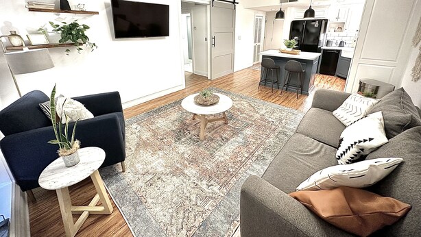 A modern living room with a sofa, a coffee table, and a TV. There is a kitchen area with a refrigerator and a dining table.
