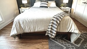 A bedroom with a large bed, two bedside tables with lamps, a wooden headboard, and a patterned rug.