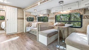 A compact RV interior with a kitchenette, a seating area, and a window offering a view of the outdoors. - Breathtaking River Retreat RV Campground - Gym, Game Room, Sauna (97530, Jacksonville, OR)