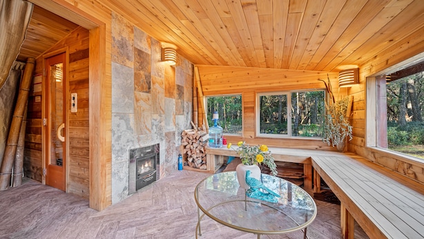 A wooden cabin interior with a glass table, benches, a fireplace, and a stone wall. - Breathtaking River Retreat RV Campground - Gym, Game Room, Sauna (97530, Jacksonville, OR)