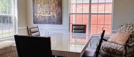 A dining area with a large table, chairs, a ceiling fan, and a window with a view of a brick building.