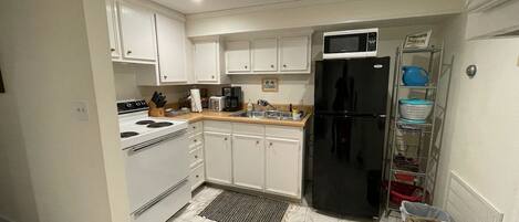 Una cocina compacta con armarios blancos, un refrigerador negro, un microondas, una estufa y un lavamanos.