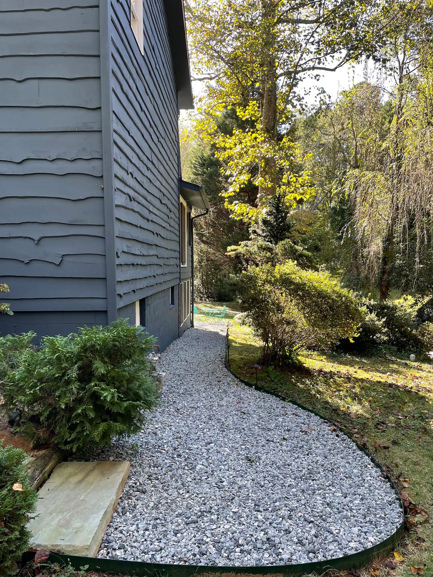 A gravel pathway leading to a house with a dark siding exterior.