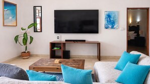 A living room with a sofa, coffee table, TV, and a potted plant. - New listing, Open air apartment,  pool, balcony & jungle view. 5 mins to beach (Sayulita)