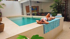 A pool area with a person lying on a ledge, a sofa, and a staircase with potted plants. - New listing, Open air apartment,  pool, balcony & jungle view. 5 mins to beach (Sayulita)