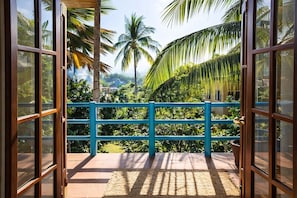 A balcony with a blue railing, a woven mat, and a view of tropical vegetation and palm trees.