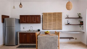 A modern kitchen with wooden cabinets, a stainless steel refrigerator, a dining table with chairs, a woven blind, and a hanging light fixture. - New listing, Open air apartment,  pool, balcony & jungle view. 5 mins to beach (Sayulita)