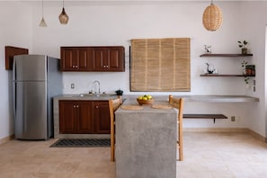 Une cuisine équipée d’un réfrigérateur, de meubles de rangement en bois, d’un évier, d’une table à manger avec des chaises et d’une fenêtre avec des stores.