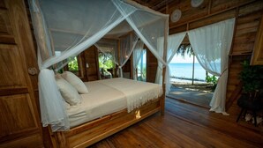 Una cama de madera con dosel, vista a la playa y piso de madera.