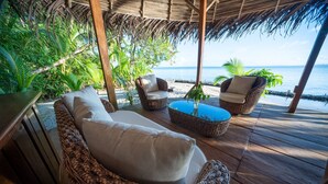 Terraza de madera con mobiliario de mimbre, incluyendo un sofá y dos sillones, con vista a la playa.
