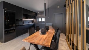 A modern kitchen with dark cabinetry, a wooden dining table, and a decorative vase. - Inviting 4-Bed Villa Lia in Vathianos Kampos (Vathianos Kampos)